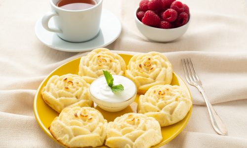 Diet cheese pancakes, rose shape, on yellow plate with tea, raspberry on textile linen napkin